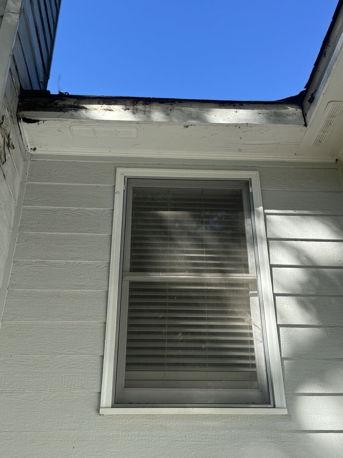 Water-damaged fascia and soffit above a window before repair